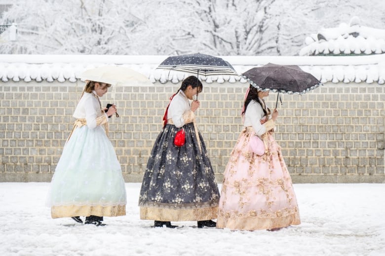 Pengunjung yang mengenakan pakaian hanbok tradisional terlihat di tengah hujan salju lebat di pusat kota Seoul.